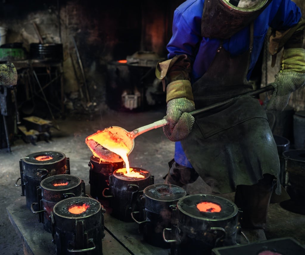 Photo d'un artisan fondeur versant du métal en fusion dans des moules cylindriques.