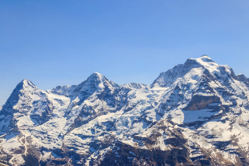 Sommets enneigés de montagne sous un ciel bleu clair, avec pics rocheux et glaciers visibles.